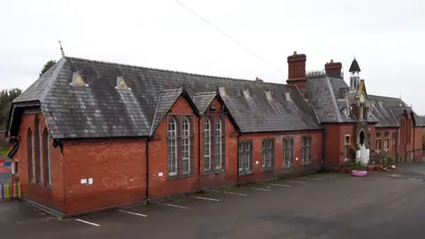 Alex Moore/LDRS A Victorian building made out of red brick with tall pointed windows and a bell tower.