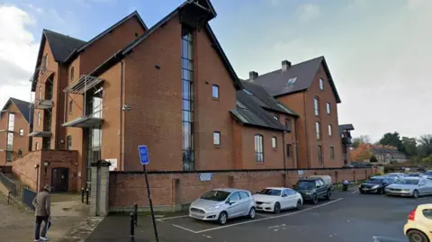 Google A large red brick building with cars parked outside