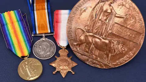 Halls A collection of three metal medals on multi-coloured ribbons and a much larger circular metal coin all sit on a dark blue background.